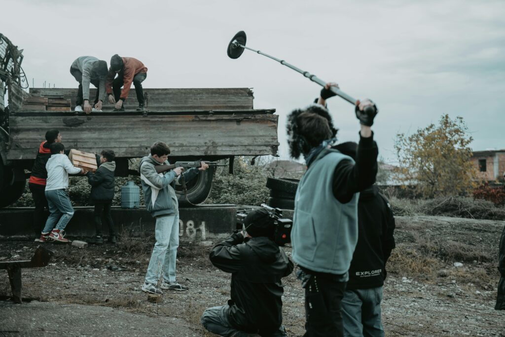 Film crew working outdoors, capturing scenes with camera and boom mic.